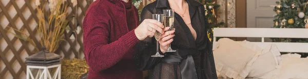 Primer plano de un par de manos sosteniendo copas de champán sobre el árbol de Navidad con luces. Gente haciendo un brindis. Copas de champán en manos sobre fondo dorado. Concepto de fiesta y celebración. Banner web — Foto de Stock