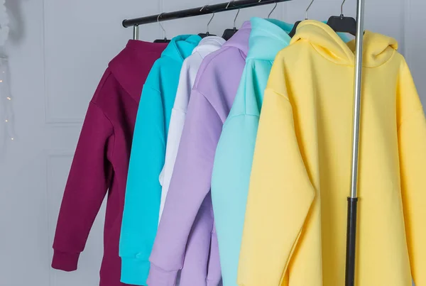 Hoodies multicoloridos em cabides em uma loja de esportes de perto, conceito de roupa. Fila de diferentes camisas com capuz, manga comprida, suéter em hangers.Modern show room vendendo roupas de homens, mulheres crianças. — Fotografia de Stock