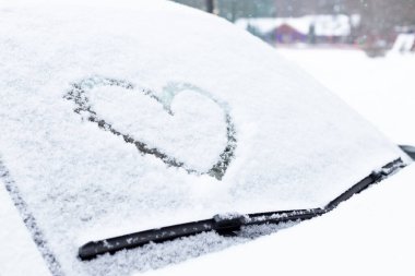 Taze kar dokusunun arka planında kalbin sembolü. Sevgililer Günü Konsepti. Kopyala uzayı. Karla kaplı bir arabanın ön camına parmak çizilmiş kalp. Yaratıcı Sevgililer Günü.