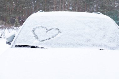 Taze kar dokusunun arka planında kalbin sembolü. Sevgililer Günü Konsepti. Kopyala uzayı. Karla kaplı bir arabanın ön camına parmak çizilmiş kalp. Yaratıcı Sevgililer Günü.