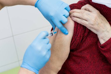 Elinde şırınga tutan ve yaşlı hastaya iğne yapan koruyucu eldivenli bir doktor. Yaşlı aşılar konsepti. Yaşlı bir hastayı grip, grip, zatürree ya da