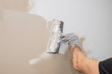 Duvarda sıva yapan inşaatçı işçilerin eli. Tadilat işçilerinin elleri duvarın alçıya alınması. İnşaat işleri tamamlanıyor. Spatül duvarı ile aynı hizada.