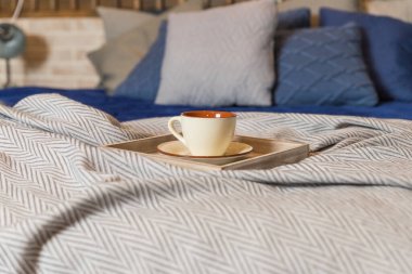Kahve fincanı ya da sabah yatağın üstünde sıcak çay. bej battaniye, gri ve mavi yastıklar ahşap yatakta. İskandinav iç mimarisi. Kupaya odaklan.