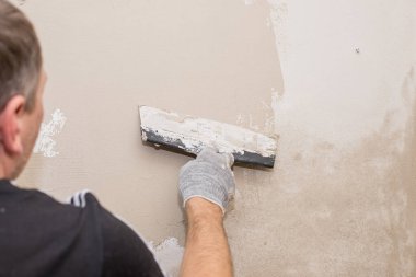 Duvarda sıva yapan inşaatçı işçilerin eli. Tadilat işçilerinin elleri duvarın alçıya alınması. İnşaat işleri tamamlanıyor. Spatül duvarı ile aynı hizada.