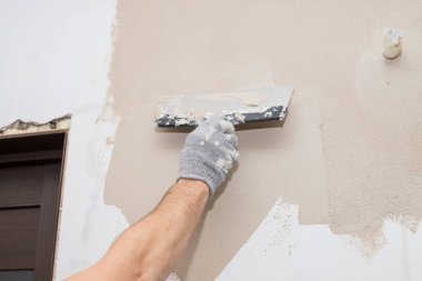 Duvarda sıva yapan inşaatçı işçilerin eli. Tadilat işçilerinin elleri duvarın alçıya alınması. İnşaat işleri tamamlanıyor. Spatül duvarı ile aynı hizada.