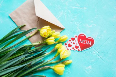 Anneler Günü için bir buket nergis, zarf ve kırmızı kalple sevgili anneler günü konsepti. Taze bahar çiçekleriyle birlikte kartpostal. Boşluğu kopyala.