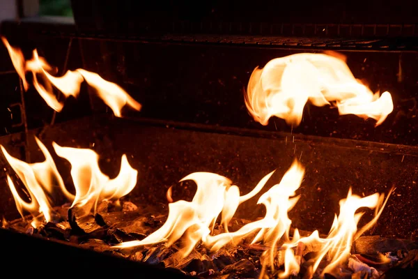 Hot churrasco Grill e queima de fogo. Você pode ver mais churrasco, comida grelhada, chamas e fogo.Grill de carvão flamejante vazio com chamas de fogo no fundo preto Closeup. Festa de churrasco ao ar livre verão — Fotografia de Stock