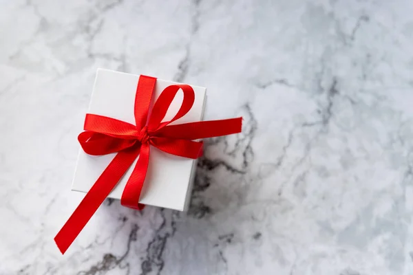 Caja de regalo blanca con lazo de cinta roja sobre fondo de mármol. vacaciones y concepto de celebración. espacio de copia. regalo para celebrar la Navidad, San Valentín o un aniversario —  Fotos de Stock