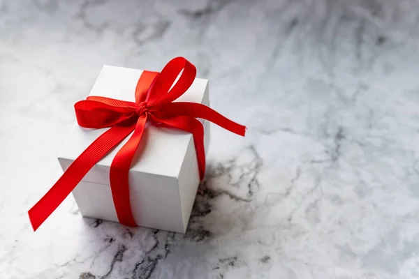 White gift box with red ribbon bow on marble background. holidays and celebration concept. copy space. present for celebrating Christmas, Valentine or an anniversary