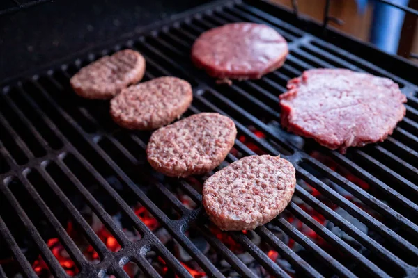 Surowe hamburgery wołowe z odrobiną soli i pieprzem na grillu. przygotowane mięso do grillowania.Surowe kotlety burgerowe.smaczne Okrągłe paszteciki surowego mięsa mielonego pieczonego na metalowej ruszcie. — Zdjęcie stockowe