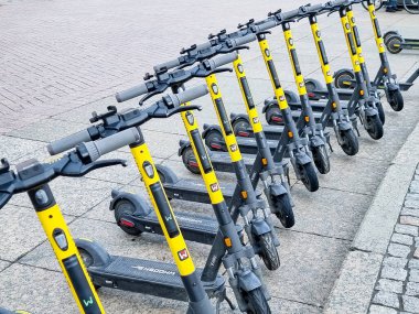 Otoparkta arka arkaya elektrikli scooterlar. Şehir bisiklet kiralama sistemi. Alternatif turizm, şehirde ulaşım, bisiklet yenileme hizmetleri. E-scooterlar bir uygulama ile kiralanabilir
