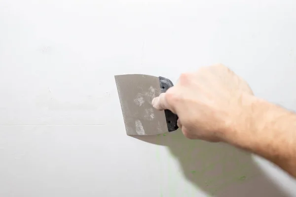 Construction worker with trowel plastering a wall.working tool, spatula in hand on a light background, work plasterer, painter, to make repairs.Hand of worker making repair in room Stock Photo