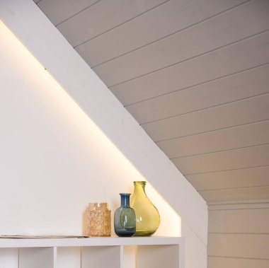 Masanın üzerinde kurumuş çiçekler, altın şişeler ve dekor olan bir vazo. İç dekorasyonun hafif duvarına karşı. Modern tarzı. Renkli cam şişeli ev dekoru