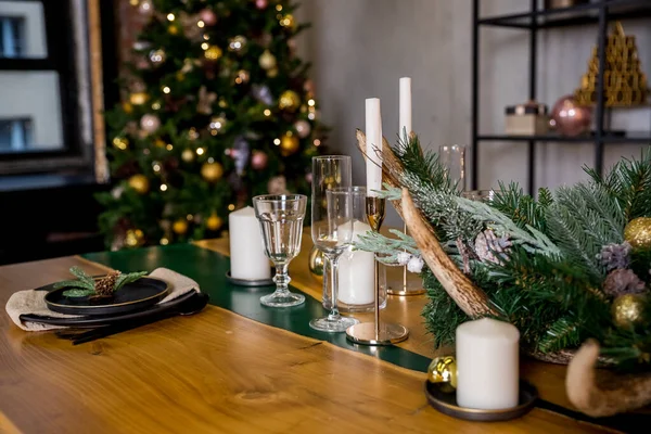 Ahşap şenlik masasında mumlar, tabaklar, bardaklar ve ekolojik süslemelerle sade bir Noel masası. Köknar dalları, altın toplar, çam kozalakları ile yeni yıl süslemeleri. Sıcak kış tatili.