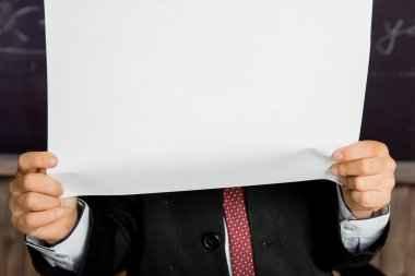 Okul tahtasının üzerinde boş defterleri tutan eller. Boş yer, okul defteri, günlük sunum şablonu. Oğlan boş beyaz kağıdın arkasında, reklam kurulunda. Okul yılının başında.