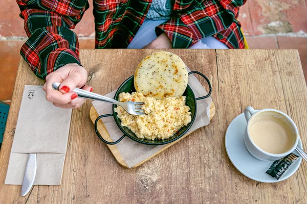 a female model wth red nail polish tucking into a colombian style scrambled eggs with corn bread and a coffee birds eye view 