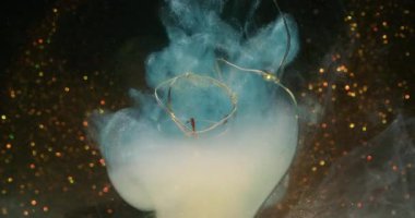 Haze akışı bulanık. Kırık ampul. Fişek çelengine renk buharı dökülmüş. Işıltılı koyu arkaplanda mavi beyaz duman boyası kıvrılır..