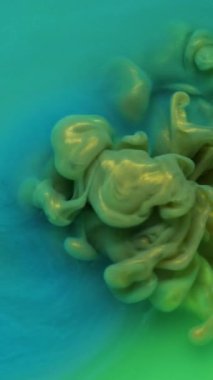 Dikey video. Renkli duman dokusu. Suyu boya. Odaklanmamış mavi yeşil bulut soyut arkaplanda egzoz parlatıcı sıvısı sıçratır.