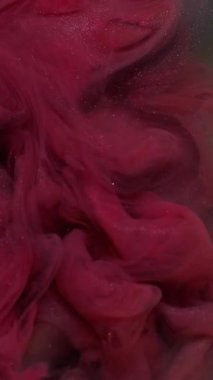 Dikey video. Parıltı sıçraması. Mürekkebi karıştır. Bulanık pembe, mor, sarı renkli su soyut karanlık sanat arka planında süzülen parlak parçacıklar..