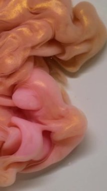 Dikey video. Mürekkep girdabı. Renk bulutu. Soyut beyaz arkaplan üzerinde odaksız pembe, altın sarısı, akrilik, simli duman dokusu.