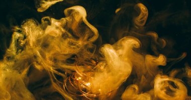 Pigment bulanıklığı. Parlak duman dalgası. Sarı altın parıldayan sis karışımı mürekkep sıvıda. Açık çelenk rengi soyut siyah arkaplan.