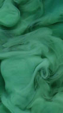 Dikey video. Mürekkep girdabı. Renk bulutu. Odaklanamayan yeşil sıvı akrilik kimyasal duman soyut koyu siyah arkaplanda yayılıyor..