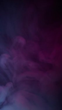 Dikey video. Duman girdabı. Boya buharı. Siyah arkaplana dökülen mavi mor buhar pigmenti. Soyut sanat sıvısı. Odaklanmış su sıçraması..