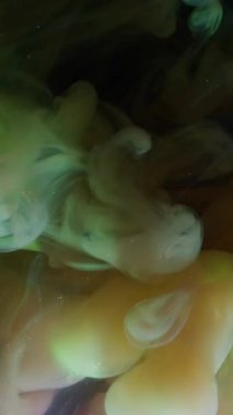 Dikey video. Bulut mürekkebi. Parıldayan sis. Parlak duman patlaması siyah arkaplanda renk pigmentini karıştırıyor. Sarı yeşil soyut parıltı sihirli akışı.