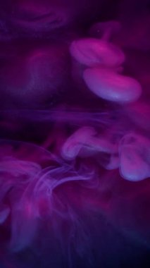 Dikey video. Renkli sis. Pigment dalgası. Neon mor mor boya suda çözünüyor. Siyah arkaplanda parlayan duman soyut odaklanmış karışım.