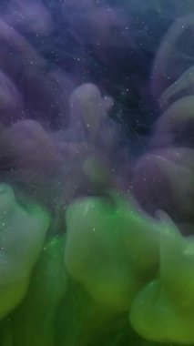 Dikey video. Hipnoz sıvısı. Renkli sis. Siyah arka planda yeşil mor bir girdap var. Mürekkep karışımı titreşen parçacıklar çözünmüş sıvı.