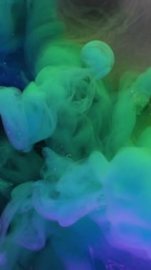 Dikey video. Duman patlaması. Boya akışı. Mor gri arka planda mavi yeşil sıvı sis dalgası spreyi. Renkli neon rengi soyut pigment karışımı bulanıklığı.