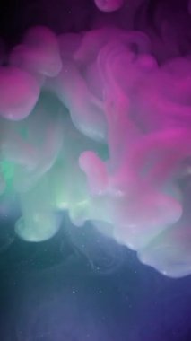 Dikey video. Bulut sıçraması. Neon mürekkebi. Mor yeşil dumanlı patlama. Parlayan sıvıyla harmanlanmış renk. Siyah soyut odaklanmış arkaplan.