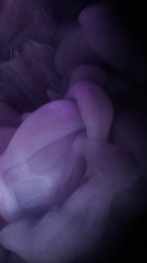 Dikey video. Bulut mürekkebi. Parıldayan sis. Parlak sis emülsiyonu bulanık siyah arkaplanda renk pigmentini harmanlıyor. Mor gri soyut akış.