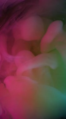 Dikey video. Hipnoz sıvısı. Renkli sis. Pembe yeşil neon bulutu siyah arkaplana yayılıyor. Mürekkep karışım parlaklığı çözünmüş sıvı.