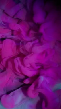 Dikey video. Duman patlaması. Boya akışı. Arka planda parlak pembe sisli dalga spreyi. Renkli soyut pigment karışımı siyah bulanıklık.