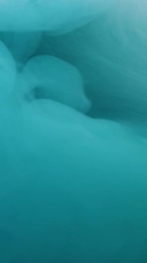 Dikey video. Sis dalgası. Sis mürekkebi kıvrılıyor. Sanatta karıştırılmış mavi cyan boyası çözünmüş sıvı. Hipnotik akış hareketi renk soyut arkaplan.