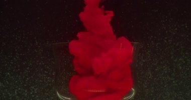 Kırmızı sıçrama. Doldurulmuş cam. Odaklanamayan renkli mürekkep dalgası su pigmenti soyut koyu siyah arkaplana yayılan girdap buharı.