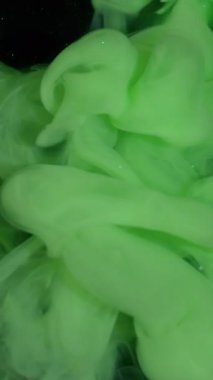 Dikey video. Duman akıntısı. Boyayla boyanmış. Parlak yeşil boya akışı. Sanat dumanı spreyi soyut bulanık siyah köpüklü su arka planı.
