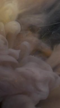 Dikey video. Duman patlaması. Buharı boya. Siyah sarı renkli pigment dalgası soyut bulanık siyah arkaplanı harmanlıyor. Buhar girdabı fantezi köpüklü boya.