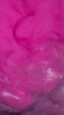 Dikey video. Işıldayan sıvı. Boya girdabı. Parıldayan sanat parçacıkları su akar. Neon rengi emülsiyon patlaması pembe beyaz gümüş soyut arkaplan.