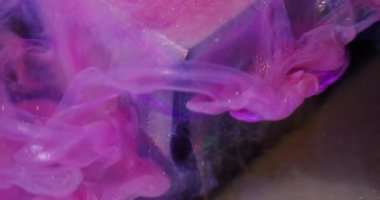 Sızdıran sim. Odaklanmamış sanat sıçraması. Pembe parlak mor akış küpü. Suyun soyut arkaplanındaki parlak renk boyası çözülüyor.