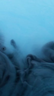 Dikey video. Duman patlaması. Duman boyası. Mavi suda siyah dalga pigmenti döküldü. Renk akışı çözünmüş boya soyut arkaplanı çözer.