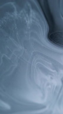 Dikey video. Mürekkep değişimi. Pigment eridi. Beyaz yuvarlak kütle gri sıvıda yayılıyor. Grunge sanatı akışı soyut odaklanmış siyah arkaplan ortaya çıkardı.