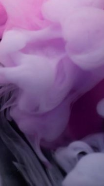 Dikey video. Sis dalgası. Buhar mürekkebi. Siyah arkaplana yayılan beyaz pembe sıvı girdap. Bulanık renk soyut ışıldayan pigment suyun altında yüzüyor.