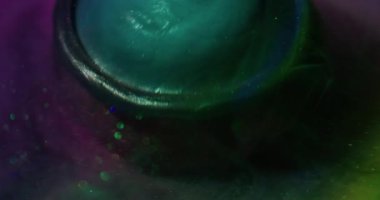 Parlak bir damla. Bulanık sıvı karışımı. Yuvarlak kürede yeşil mavi sıvı dökülmesi. Suyun altındaki renk pigmenti soyut mor arkaplanı çözüyor.