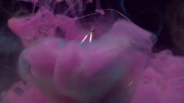 Odaklanmamış duman damlası. Parlayan ampul. Aydınlatılmış cam çelenk soyut renk sıçraması. Siyah arkaplanda pembe mavi bulut akışı.