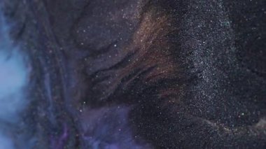 Parıldayan mürekkep. Işıl ışıl. Soyut akrilik zemin üzerinde odaksız mor turuncu renkli simli parçacıklar koyu siyah pigment.