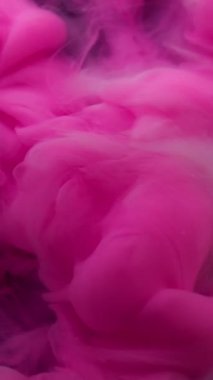 Dikey video. Karışım akışı. Atmosferik duman. Soyut koyu siyah arkaplana yayılan, suda dönen dumandaki pembemsi mavi mürekkep..