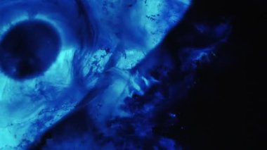 Mürekkebi karıştır. Sıvı dökülmesi. Odaklanmamış mavi renk su esansı soyut koyu siyah sanat ışığı arka planına neon boya damlası dök.