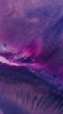 Dikey video. Parıltı akışı. Renk parçacıkları. Soyut akrilik zemin üzerinde akan mor renkli parlak lekeler..